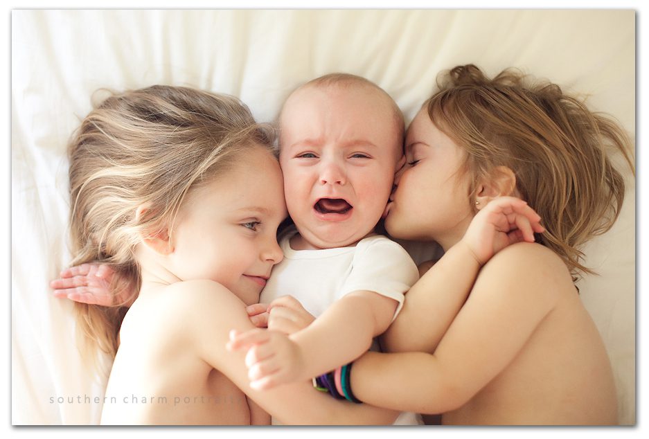 it's not easy being the little brother, baby brother squooshed and kissed by two big sisters, crying baby boy six months