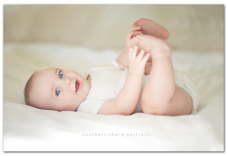 six month old grabbing toes chubby legs and white sheets