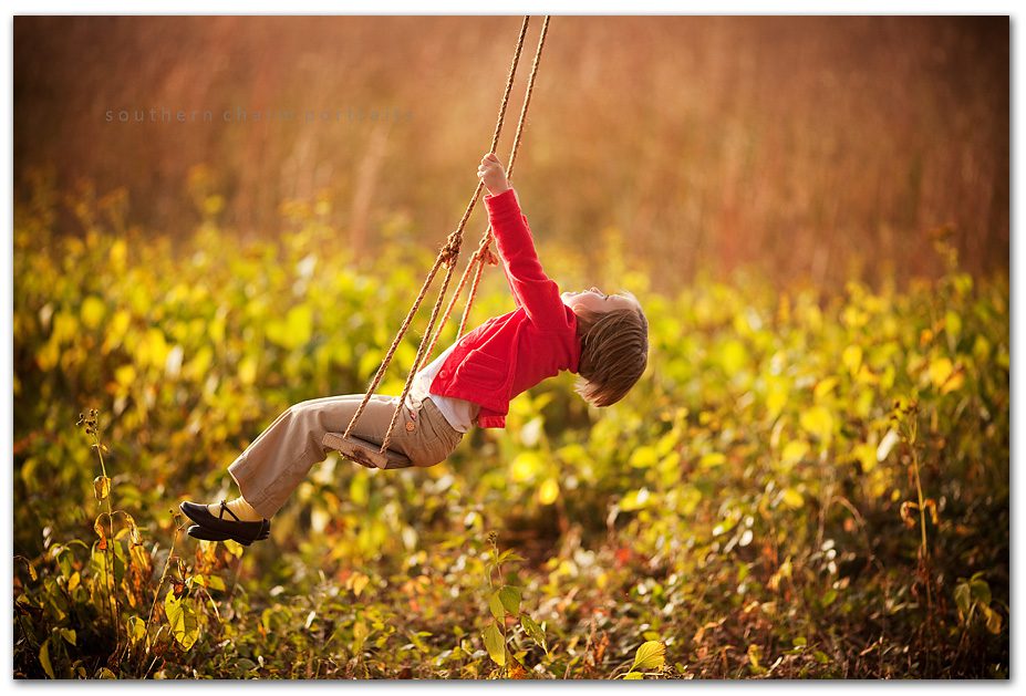 child laying back in swing having so much fun young child red sweater