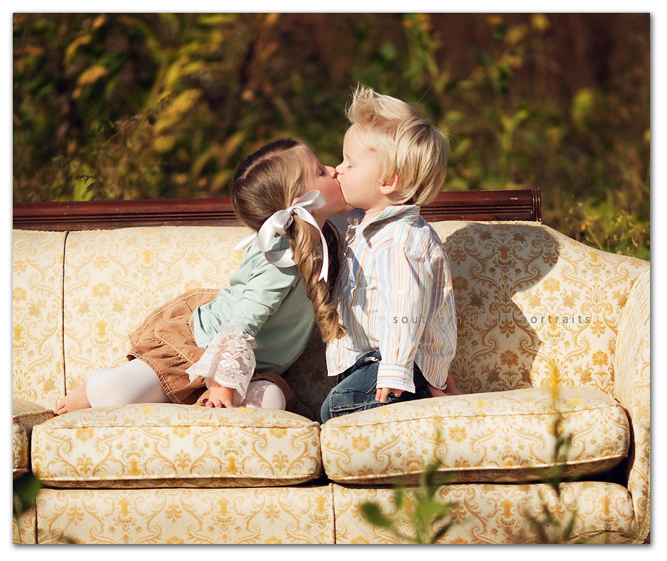 brother and sister sitting on antique couch giving a smooch spiked hair and pig tails