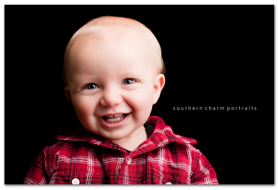 baby in red plaid holiday shirt with black backdrop and big smiles