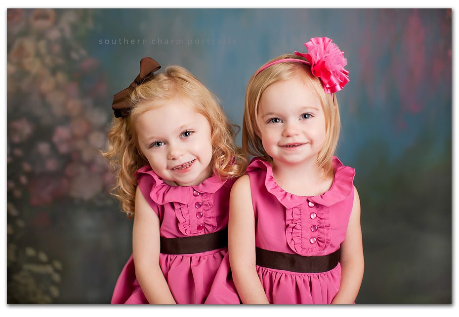 blonde headed little sisters with blue eyes and pink dresses sitting side by side