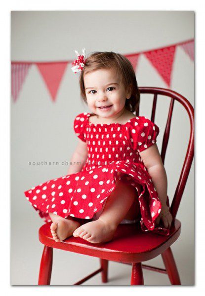 child smiling with red polka dot dress on in red child sized chair