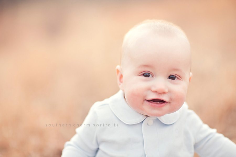 a six month old baby boy sitting in field smiling with a little tooth showing through