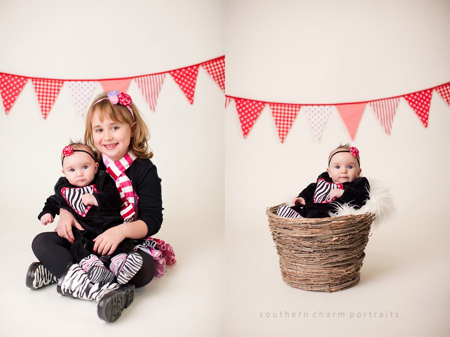 big sister holding baby sister in valentine's day clothing with bunting banner in background