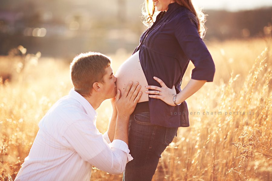 daddy kissing mommy's pregnant belly in field with tall grass