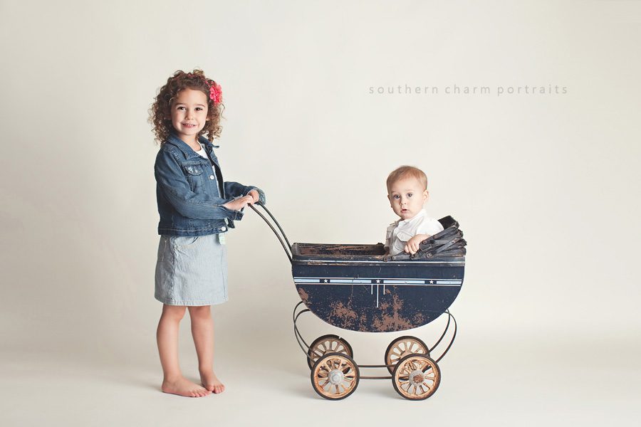 big sis pushing little brother in baby carriage in portrait studio