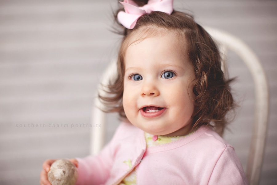 baby girl sitting in chair with pink cardigan and hairbow