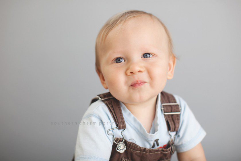 little boy in overalls smiling with big blue eyes